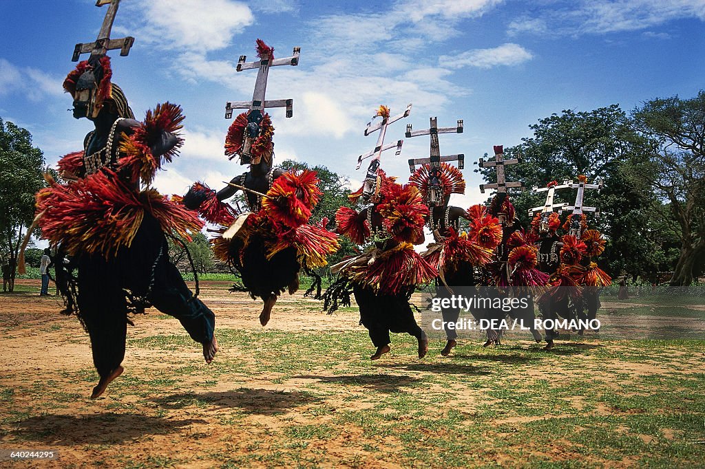 Masked Dogon dancers performing funeral ceremony beneath sandstone cliffs in Mali
